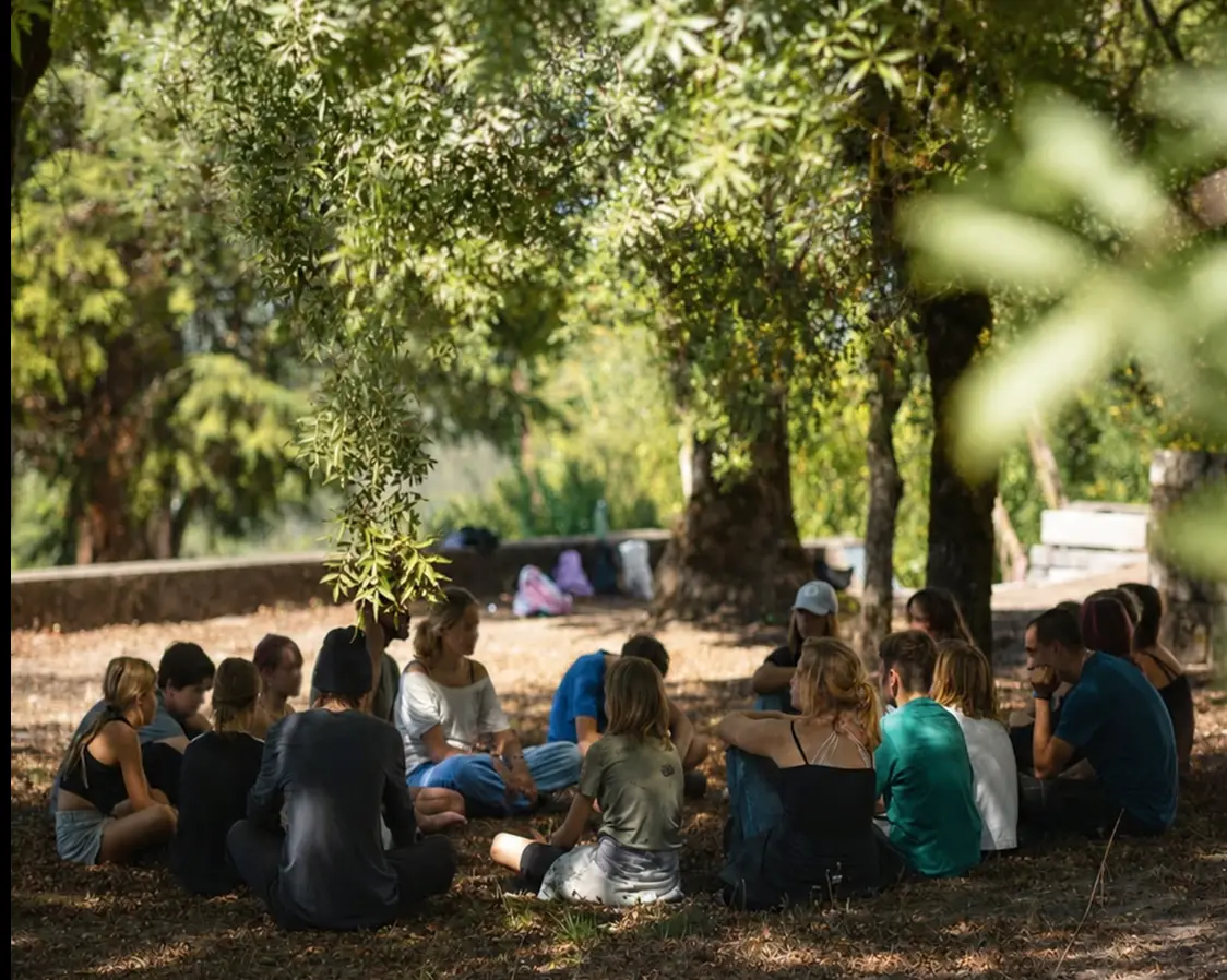 Young people and adults sitting in a circle under the trees at Waterfall Valley.